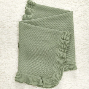 Sage green ruffle trim knitted baby blanket made of soft cotton on white fur background