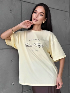 Detail of light yellow cotton T-shirt featuring Saint Tropez print on textured gray backdrop