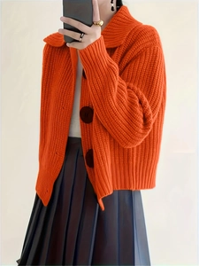 Detailed close-up of bright orange knit cardigan featuring chunky texture and black buttons