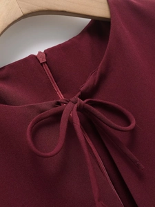Detail of burgundy dress featuring a back zipper and elegant self-tie bow at the neckline