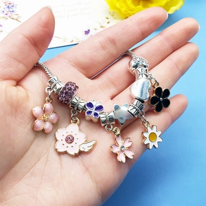 Detail view of a beaded bracelet with pink enamel flower charms and peace letter beads