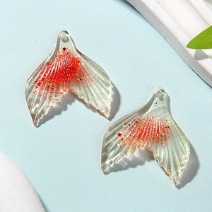 Detail of transparent resin mermaid tail charms with red glitter for DIY jewelry making