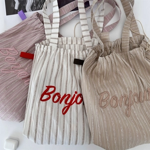 Detailed embroidery of 'Bonjour' on multi-color striped canvas tote bags in a soft layout