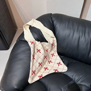 Beigefarbene Stricktasche mit rotem Schleifenmuster und Karos auf schwarzem Ledersofa