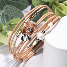 Macro detail of layered leather wrap bracelet with rose gold floral charms and a pearl