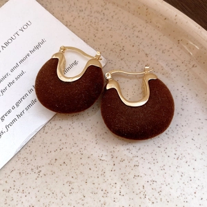 Detailed close-up of brown flocked U-shaped earrings with gold alloy clasps on ceramic