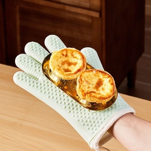 Mint green silicone oven mitt with heart texture holding a golden tray of egg tarts
