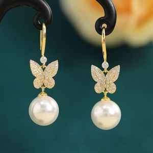 Macro shot of gold butterfly earrings with pave zircon and white round hanging pearl