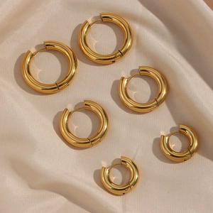 Three pairs of thick gold hoop earrings in graduated sizes on pink silk background