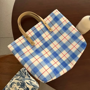 Close-up of blue plaid tote bag featuring brown leather handles and metal rivet details