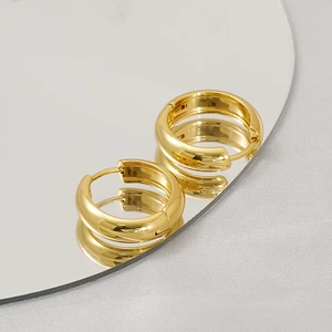 Polished gold geometric U-shaped hoop earrings on a reflective mirror surface