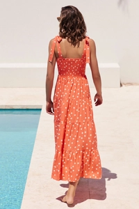 Outdoor poolside view of a tiered orange polka dot maxi dress with bow shoulder straps