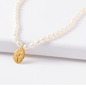 Macro detail of natural pearl necklace with rose engraved gold coin oval pendant