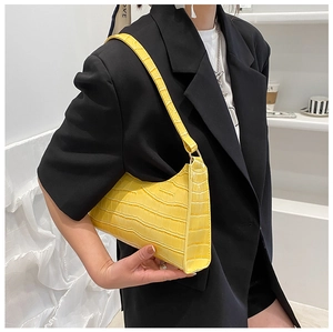 Detail of yellow crocodile pattern baguette bag on model wearing a black blazer