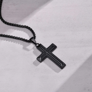 Detailed close-up of a black textured stainless steel cross pendant on a grey stone surface