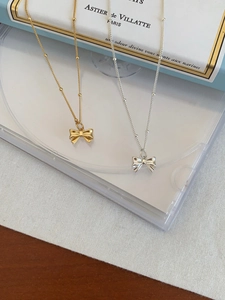 Detail of silver and gold bow necklaces on a blue book with polished metallic finish