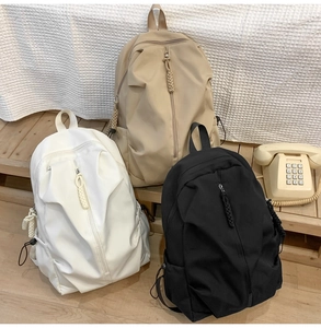 Detailed view of large capacity nylon backpacks in white, khaki, and black on wooden steps