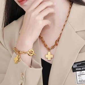 Detailed close-up of a 18K gold-plated cross pendant necklace and bracelet set on a model
