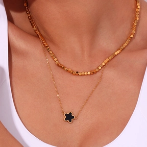 Detail of double-layer gold necklace with cube beads and black floral pendant on neck