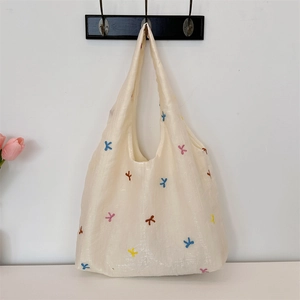 Detail of embroidered bow patterns on a cream canvas tote bag with wide straps