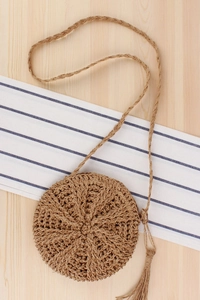 Detail of round straw woven bag featuring bohemian tassels and natural paper rope texture