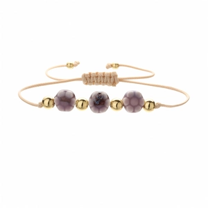 Detail of handmade woven bracelet with purple ceramic floral beads and gold metal accents