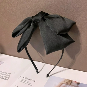 Serre-tête minimaliste en satin noir avec grand nœud sur fond de magazine