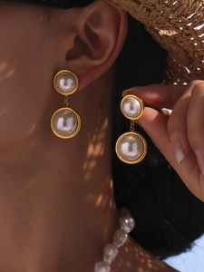 Detail of vintage French luxury gold pearl earrings worn by a model in soft sunlight