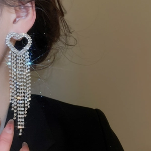 Detailed view of silver heart earrings with long crystal tassels on a model