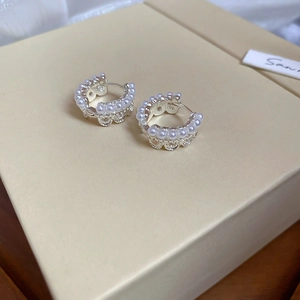 Detailed close-up of crown lace pearl hoop earrings on a minimalist jewelry box