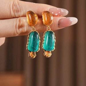 Detail of vintage oval earrings with orange and green resin gems in gold frames