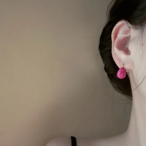 Close-up of a model wearing a bright rose pink teardrop earring with a glossy finish