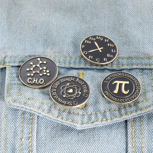 Set of four black and gold science enamel pins on denim jacket featuring atoms and symbols