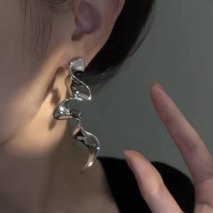 Close-up of long silver irregular wavy tassel earrings worn by a model in soft lighting