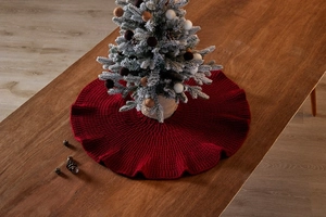 Close-up of red knitted Christmas tree skirt with ruffled edges on a rustic wooden table