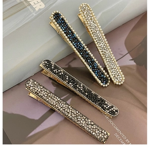 Close-up of four glittery rhinestone hair clips in silver, black, blue, and gold tones