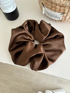 Detailed view of oversized dark brown satin scrunchie with silky pleated texture