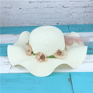 Close-up of woven straw hat with floral wreath, metal beads, and chiffon ribbon trim