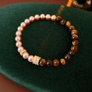 Detailed close-up of tiger eye and pink pearl beads on a green velvet jewelry stand