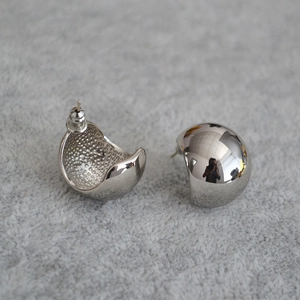 Detail view of silver spherical stud earrings showing polished finish and inner matte texture
