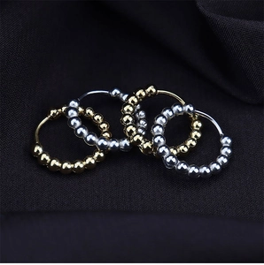 Makro-Detail von perlenbesetzten Edelstahl-Ohrringen in Gold und Silber auf Stoff