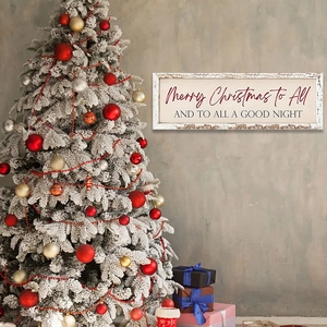 Wooden Merry Christmas wall plaque hanging on a grey wall next to a decorated tree