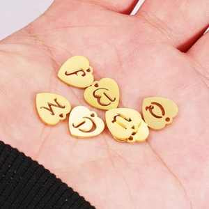 Golden 12mm stainless steel heart-shaped A-Z letter charms shown on a hand for scale