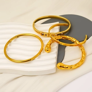 Polished gold stainless steel bangle set with engraving on white decorative stands