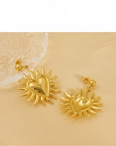 Close-up of golden sunflower heart earrings with shiny mirror finish on silk cloth