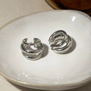 Macro view of triple layer silver ear cuffs on a white ceramic tray with linen background