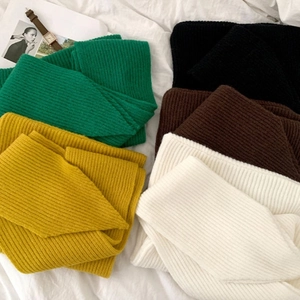 Flat lay of ribbed knit shawl scarves in green, yellow, black and white on white linen