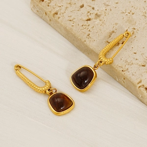 Chic gold safety pin earrings with square brown stone charms on a textured stone surface