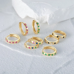 Detail view of colorful zircon huggie earrings on white textured stone background
