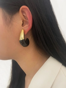 Close-up of 18K gold C-shaped earrings with black enamel detail on a fashion model